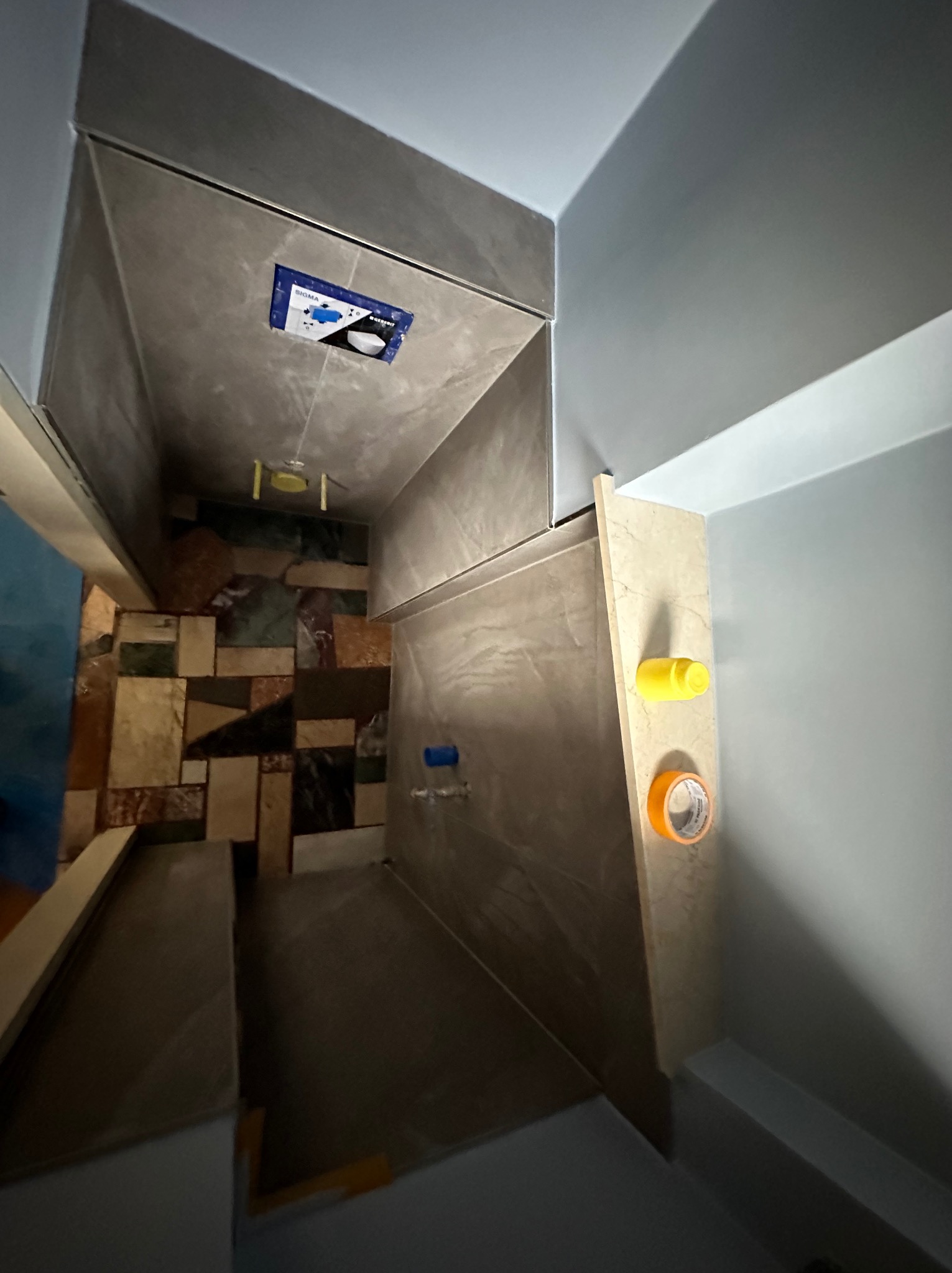 Wnętrze łazienki w trakcie prac wykończeniowych, widoczne płytki na ścianach, instalacja podtynkowa WC i akcesoria malarskie. Nietypowy układ płytek na ścianie.