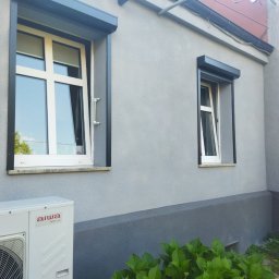 Pw Reda - Szara elewacja domu z dwoma oknami z roletami zewnętrznymi, widoczny klimatyzator i fragment drewnianego płotu.