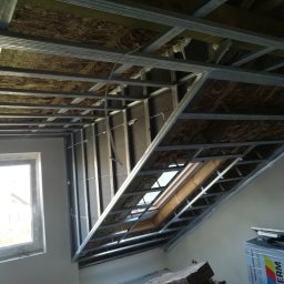 GROTBUD - Konstrukcja metalowa sufitu podwieszanego z oknem dachowym, ocieplona wełną mineralną, widok z dołu na etapie montażu.