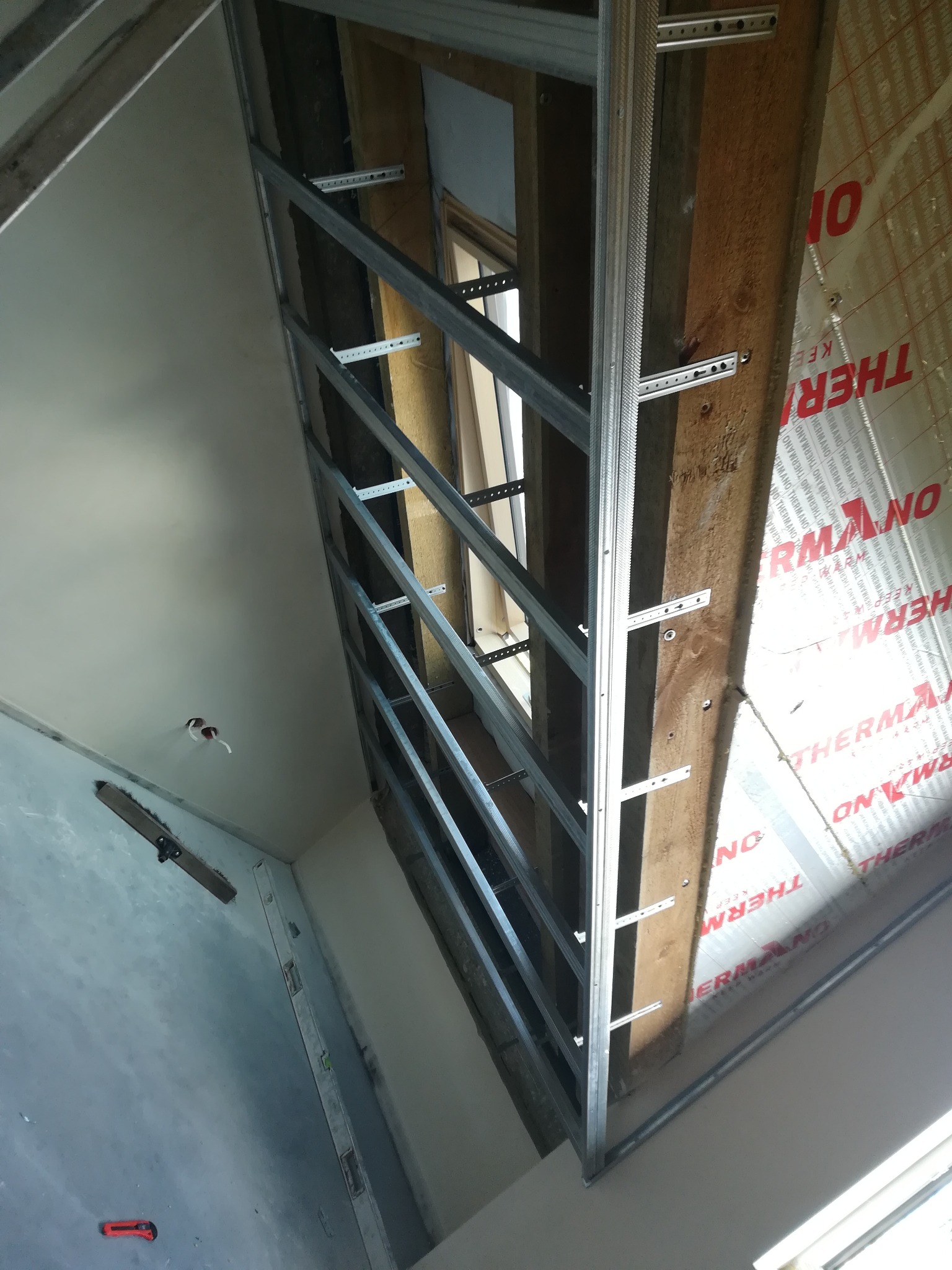 Montaż stelażu z profili metalowych do płyt gipsowo-kartonowych na ścianie z widoczną izolacją termiczną, widok z dołu.