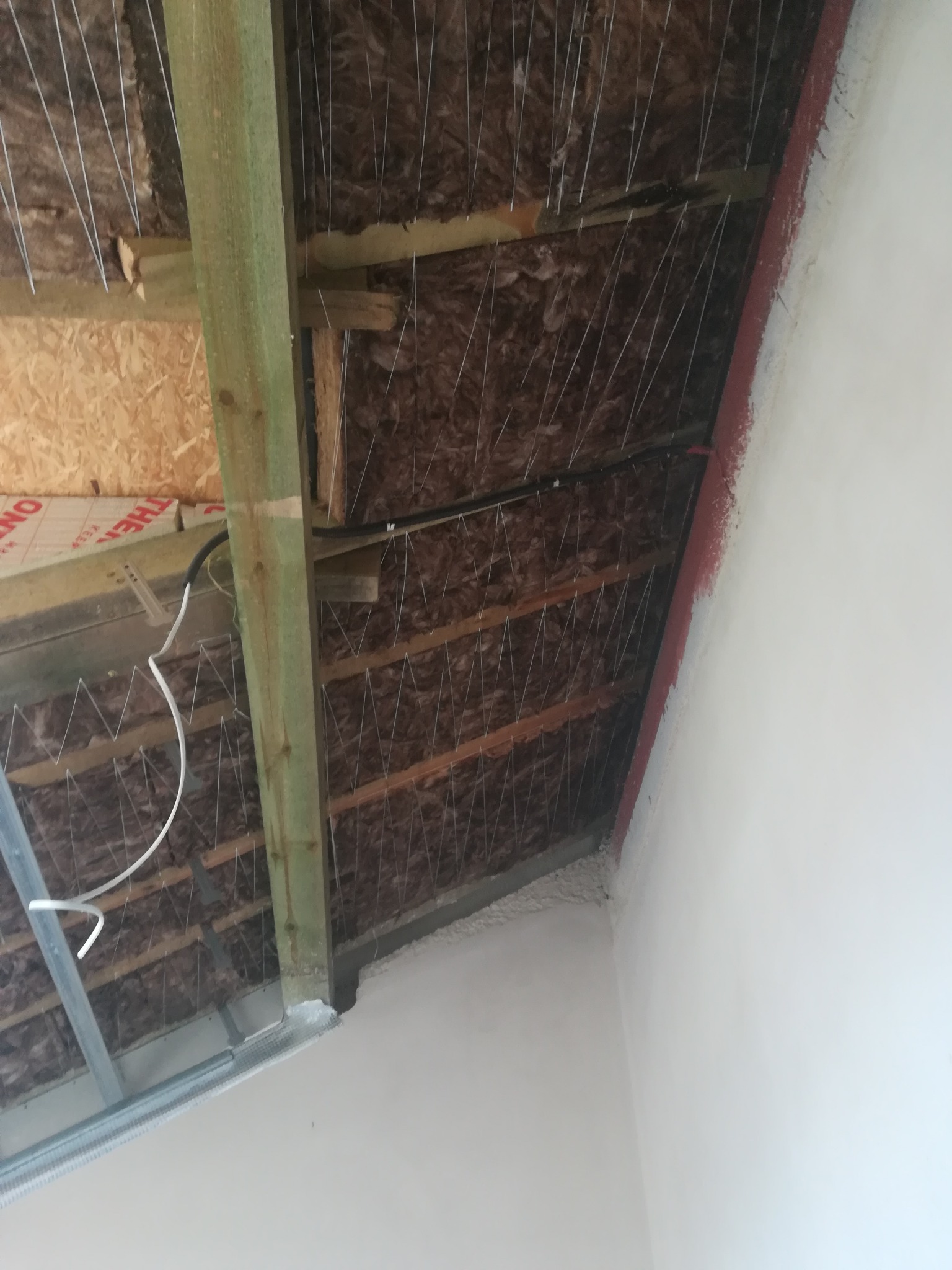 Poddasze w trakcie izolacji termicznej, widoczne wełna mineralna, drewniane belki konstrukcyjne i metalowe profile, ściana po wstępnym przygotowaniu do malowania.