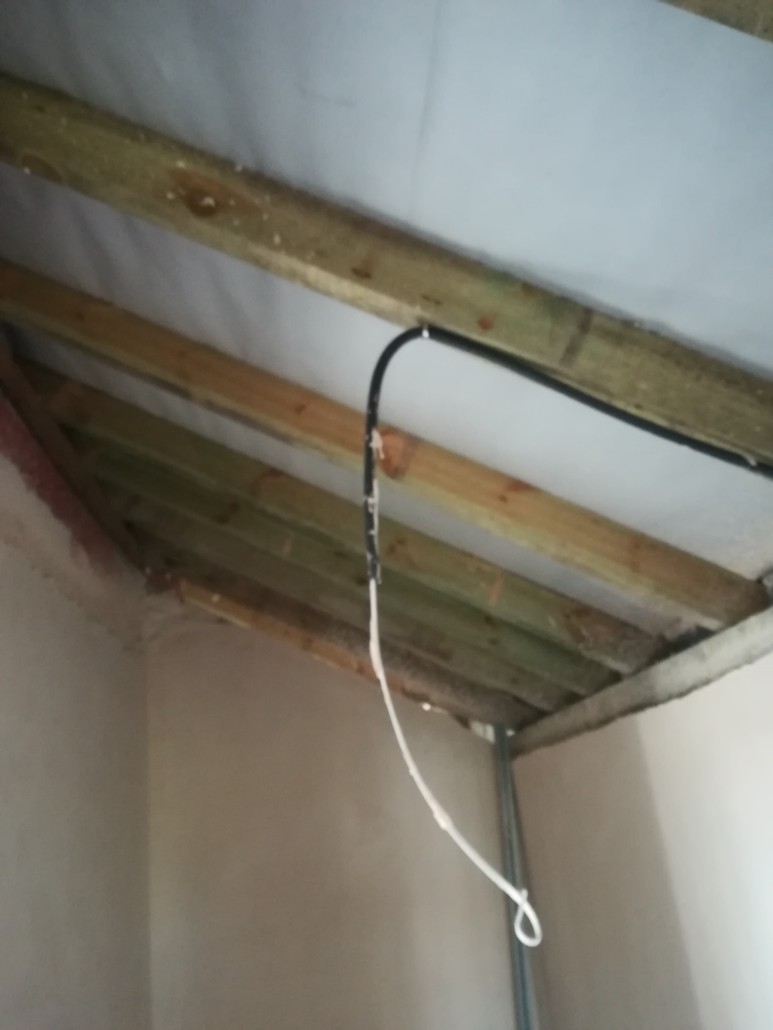 Surowy stan poddasza z drewnianą konstrukcją dachu, widoczne kable instalacji elektrycznej przed wykończeniem.