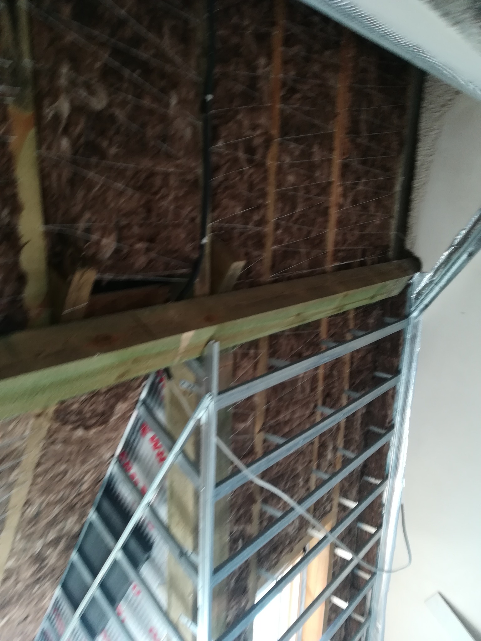 Izolacja ścian wełną mineralną z konstrukcją metalową pod płyty gipsowo-kartonowe, widoczne elementy drewniane i przewody.