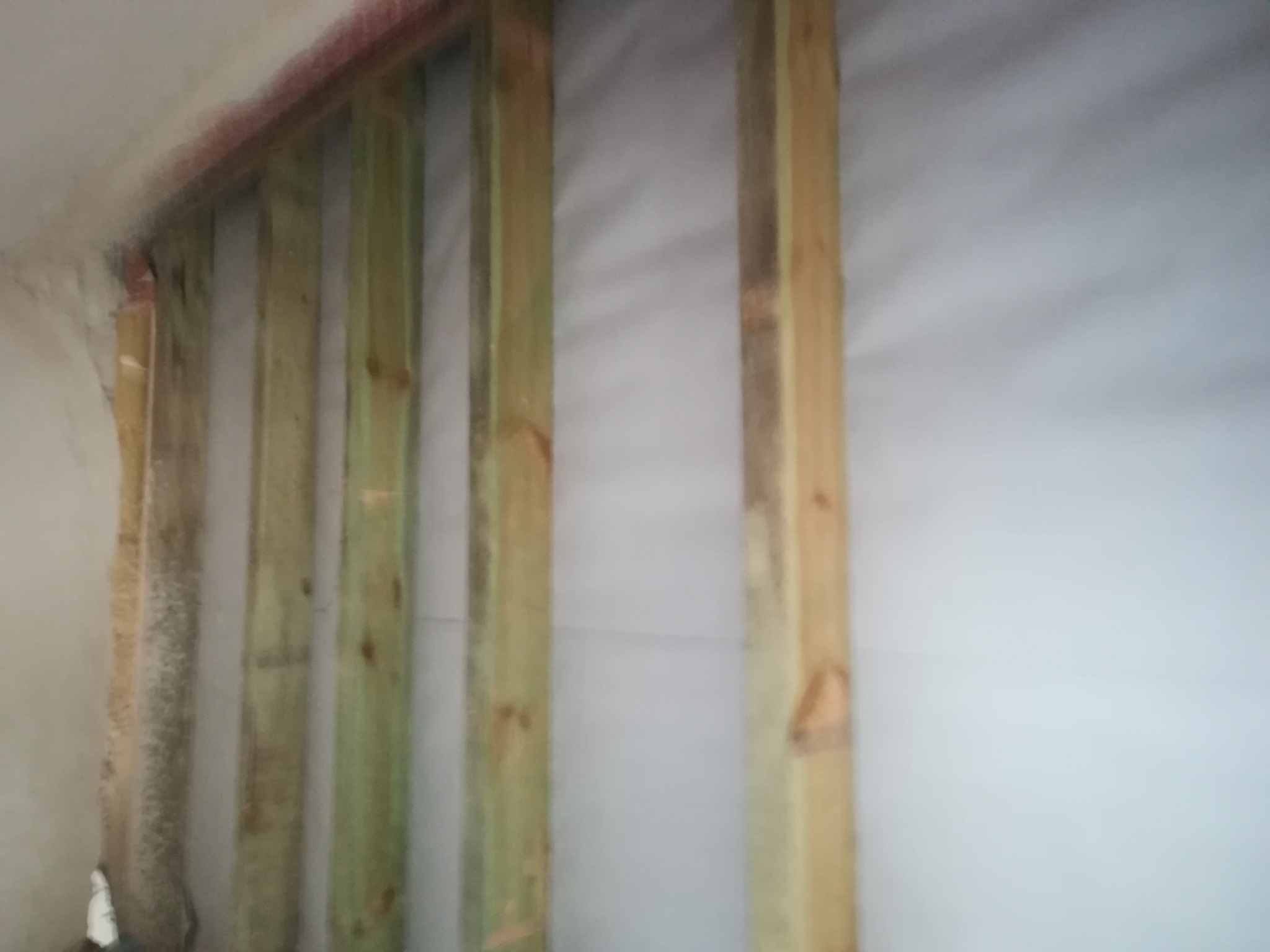 Konstrukcja szkieletowa ściany z drewnianych belek, widoczna izolacja i fragment starego tynku na ścianie, w trakcie prac remontowych.