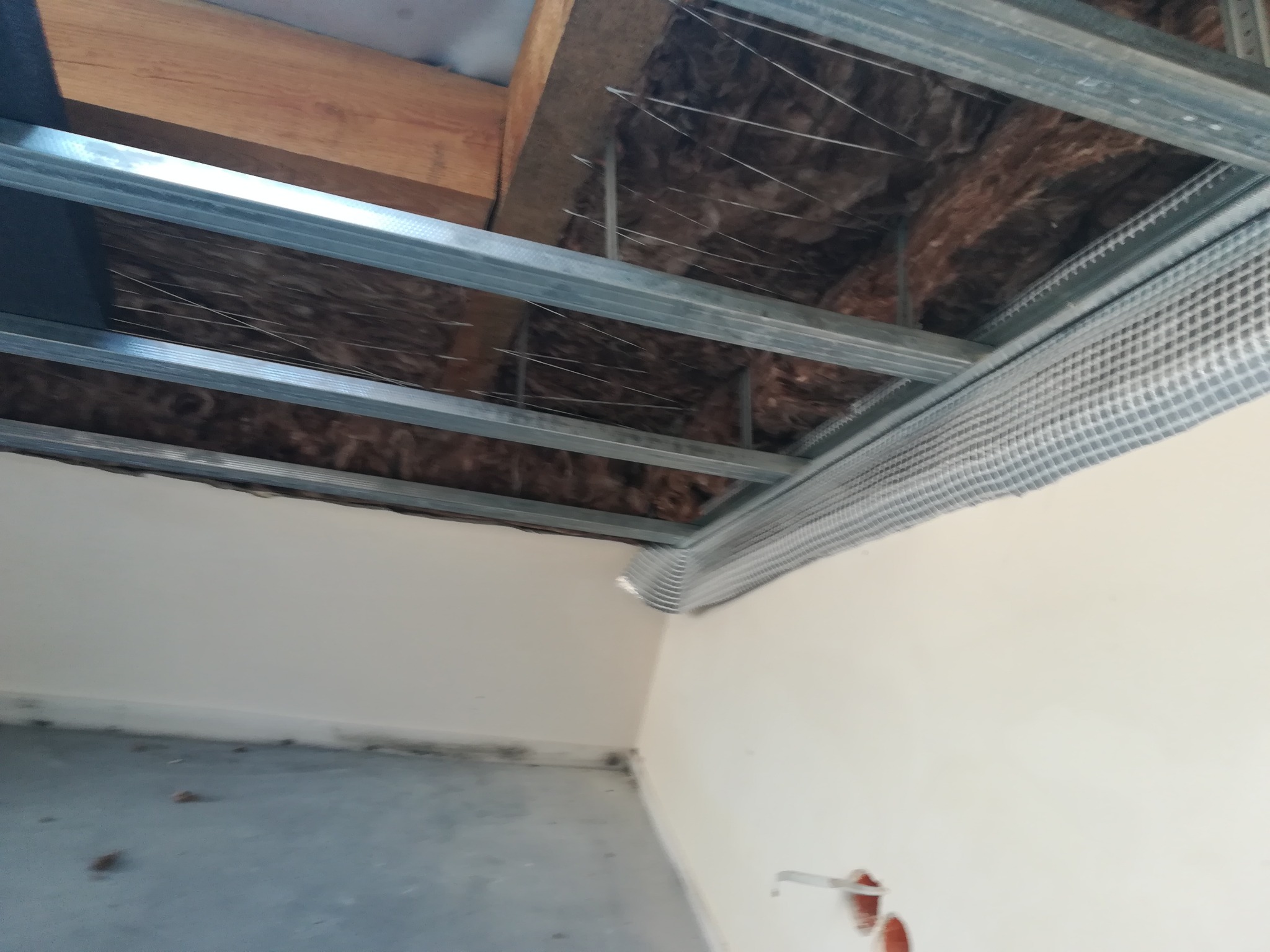 Konstrukcja metalowa sufitu podwieszanego z izolacją, widoczne profile, siatka i fragment ściany po wstępnym przygotowaniu.