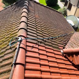 CZYSTAMOC OLEH KUSIE - Częściowo wyczyszczony dach z czerwonej dachówki, widoczna różnica między umytą a zabrudzoną częścią. W kadrze lanca myjki ciśnieniowej i fragment węża.