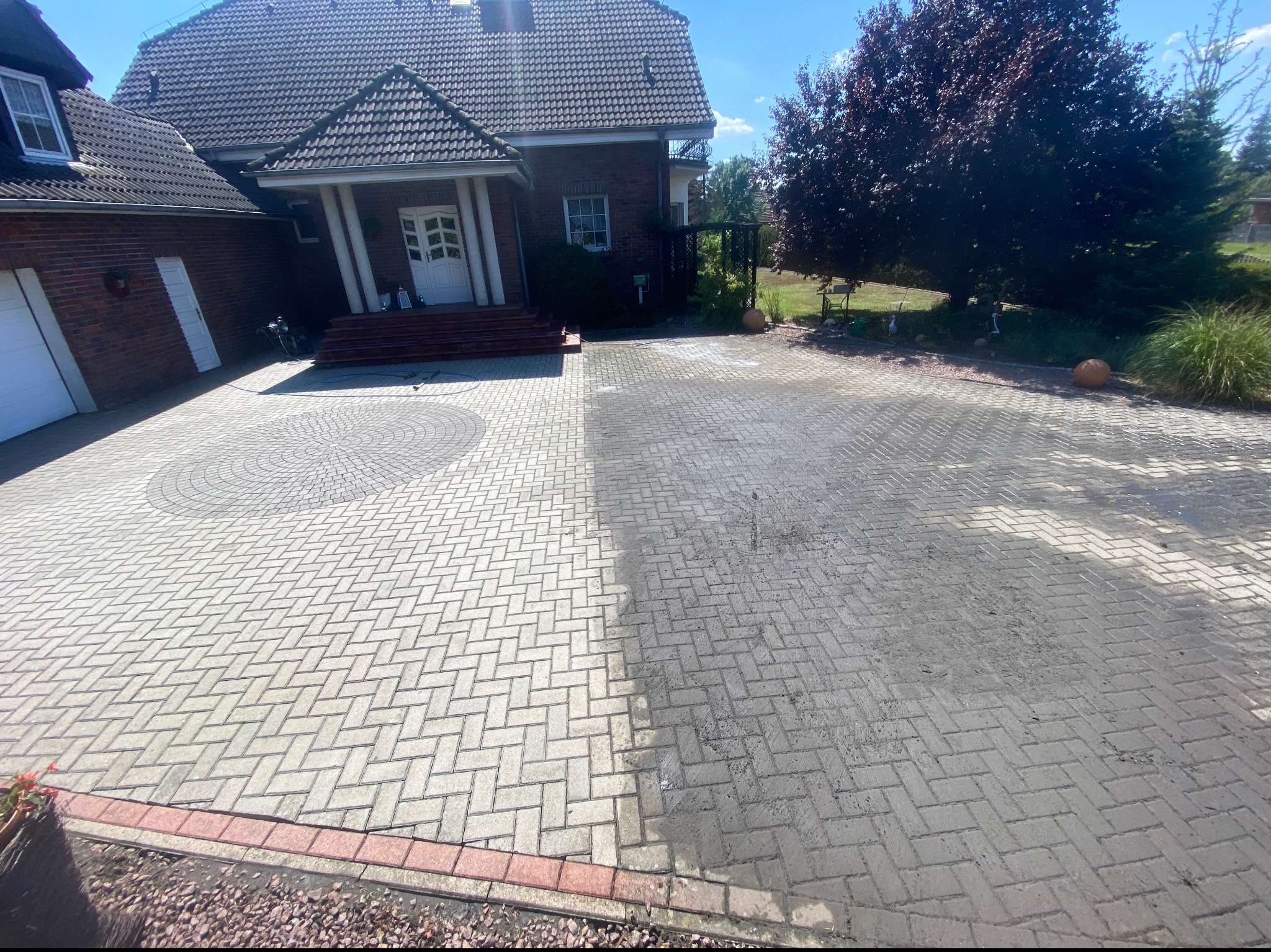 Częściowo wyczyszczona kostka brukowa przed domem w Starych Siołkowicach, widoczna wyraźna różnica między umytą a brudną częścią, na pierwszym planie czerwona obwódka z kostki.