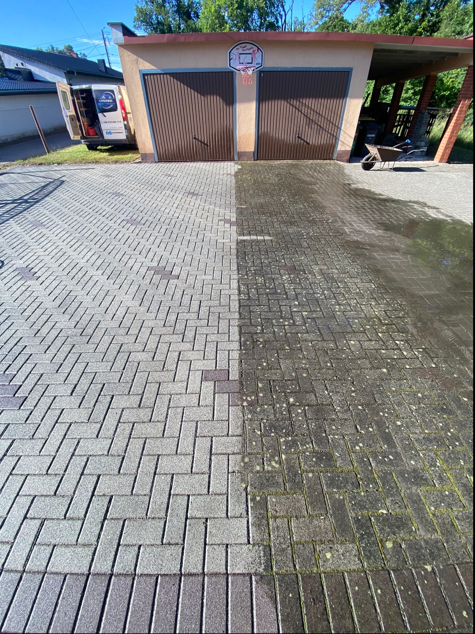 Częściowo wyczyszczona kostka brukowa przed garażem z koszem do koszykówki; po lewej stronie czysta, jasnoszara, po prawej brudna, ciemna z mchem; w tle zaparkowany biały bus firmy.