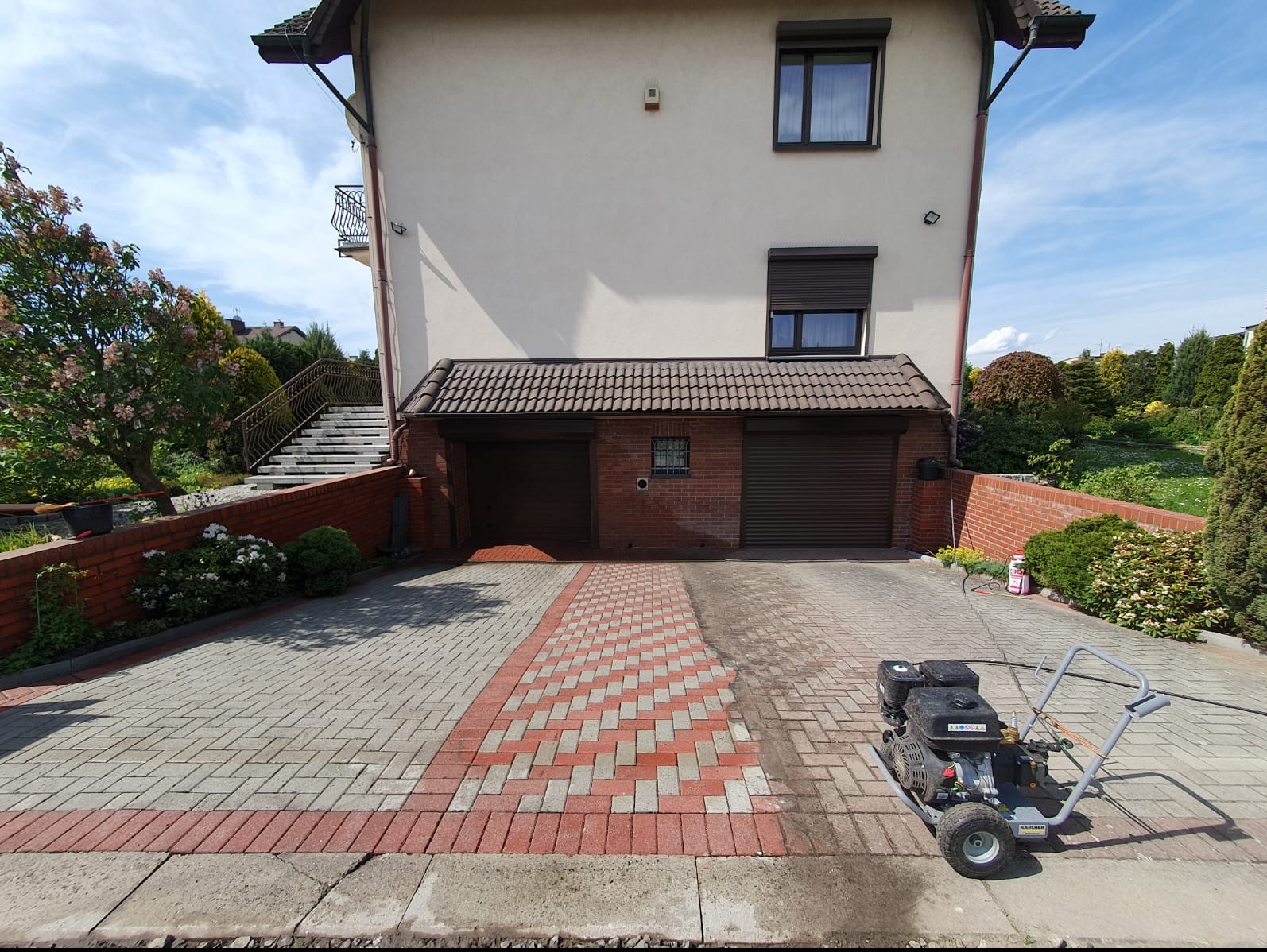 Częściowo wyczyszczona kostka brukowa przed garażem dwustanowiskowym, widoczna różnica w kolorze przed i po czyszczeniu, obok stoi myjka ciśnieniowa Karcher.