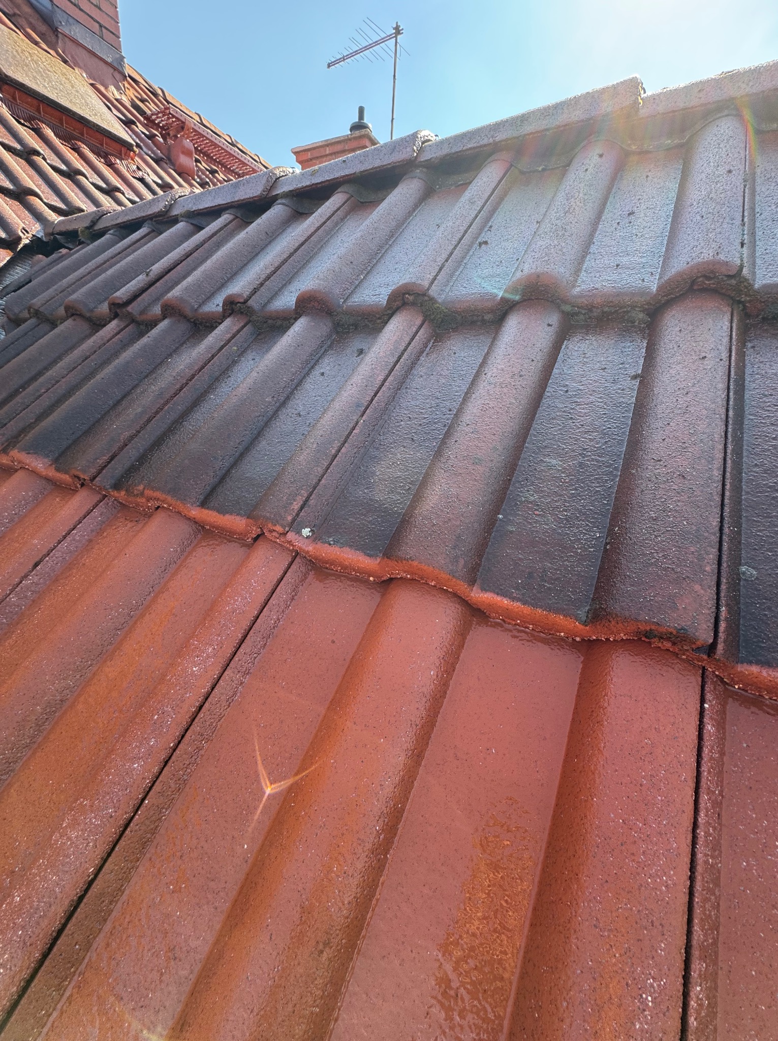 Częściowo umyty, czerwony dach z dachówki ceramicznej, widoczny kontrast czystości, antena na kominie w tle, jasne słońce.