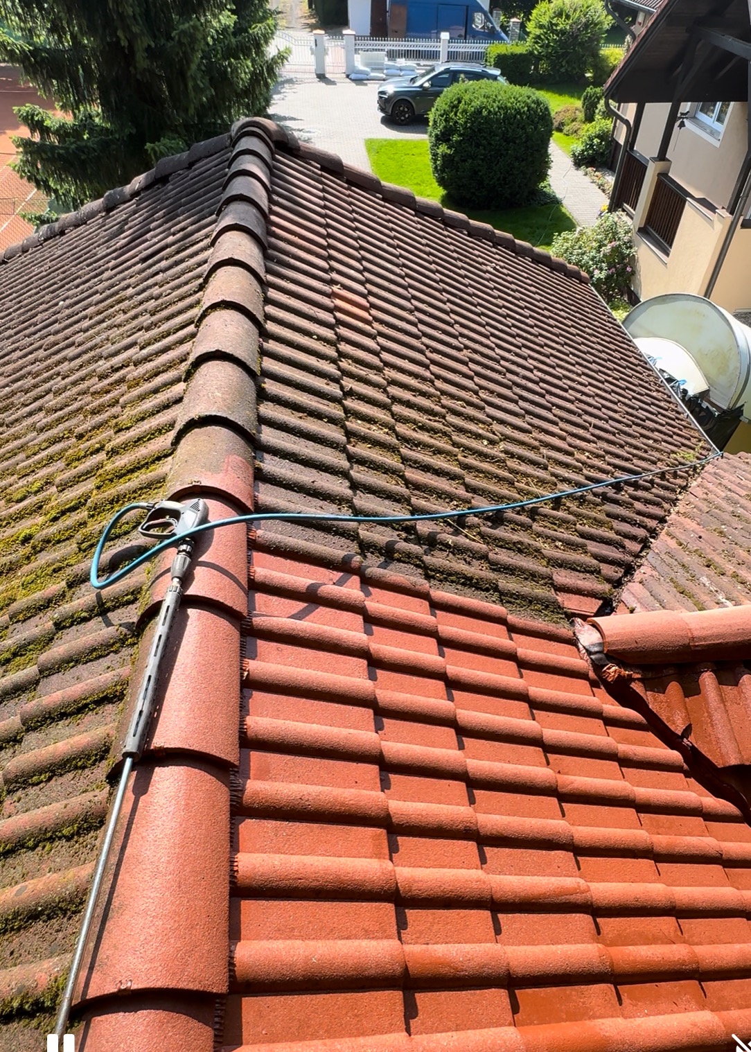 Częściowo wyczyszczony dach z czerwonej dachówki, widoczna różnica między umytą a zabrudzoną częścią. W kadrze lanca myjki ciśnieniowej i fragment węża.