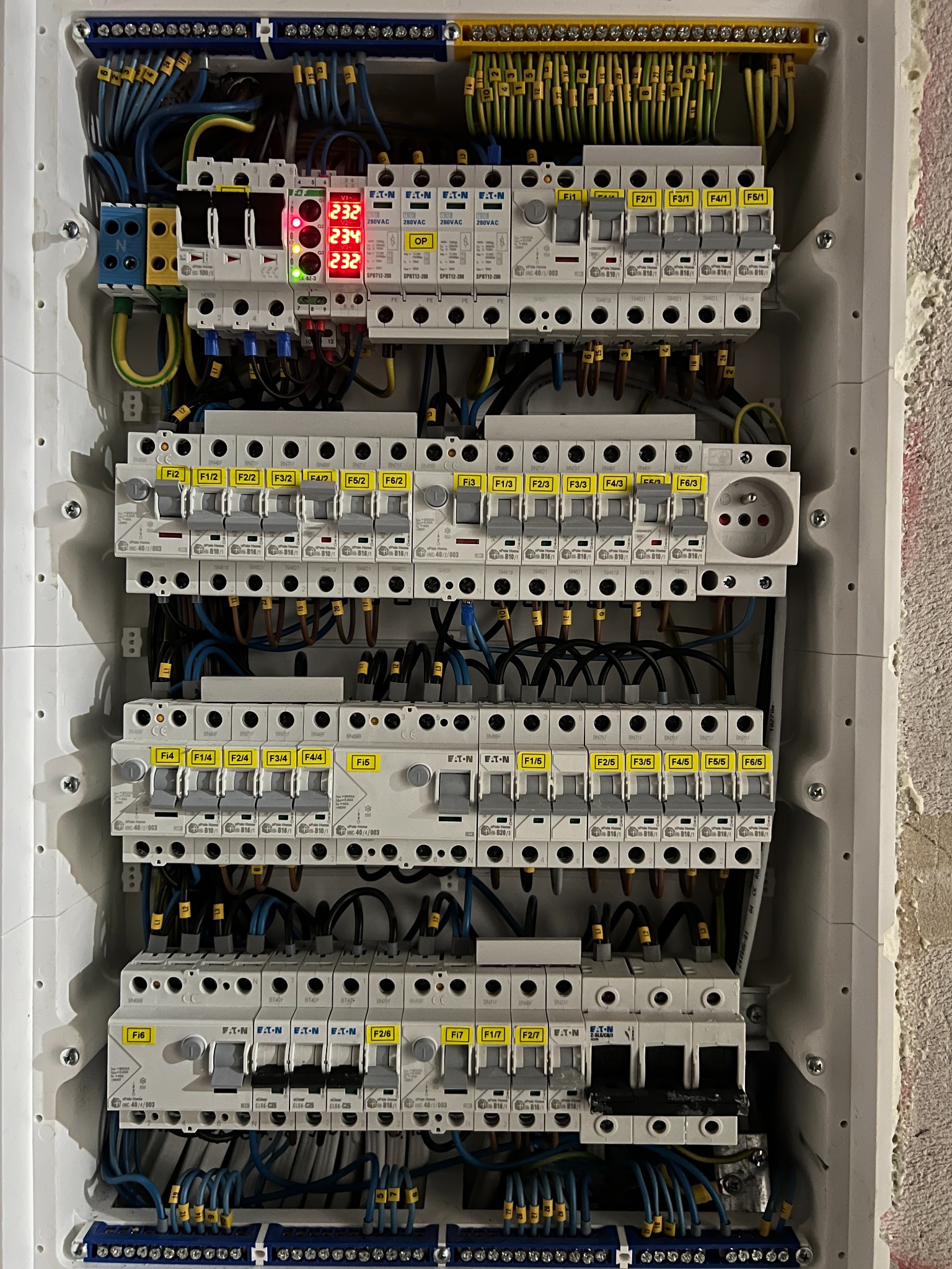 Rozdzielnica elektryczna z zamontowanymi bezpiecznikami, okablowaniem i wyświetlaczem wskazującym napięcie. Widoczne elementy instalacji elektrycznej wewnątrz obudowy.