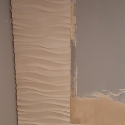 Arkadiusz Pawlak - Montaż dekoracyjnych paneli ściennych 3D w narożniku pokoju, widoczne niedoskonałości podłoża przed pełnym wykończeniem.