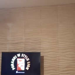 Arkadiusz Pawlak - Ściana wykończona panelami 3D o falistej strukturze, widoczne łączenia między panelami, obok otwarte drzwi, w tle telewizor i suszarka na pranie.