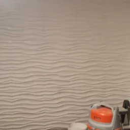 Ściana pokryta gładzią strukturalną w odcieniach bieli, z widocznym odkurzaczem budowlanym i otwartymi drzwiami do ciemnego pomieszczenia