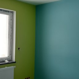 Arkadiusz Pawlak - Pomalowane na zielono i turkusowo ściany pokoju z oknem PCV marki Oknoplast, na parapecie rolka papieru, grzejnik pod oknem, widoczne puszki elektryczne bez osprzętu.