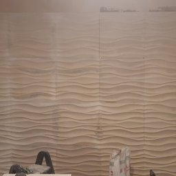 Arkadiusz Pawlak - Ściana pokryta panelami 3D o falistym wzorze, w trakcie montażu, widoczne niedokończone krawędzie i narzędzia w dolnej części kadru.