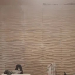 Ściana pokryta panelami 3D o falistym wzorze, w trakcie montażu, widoczne niedokończone krawędzie i narzędzia w dolnej części kadru.