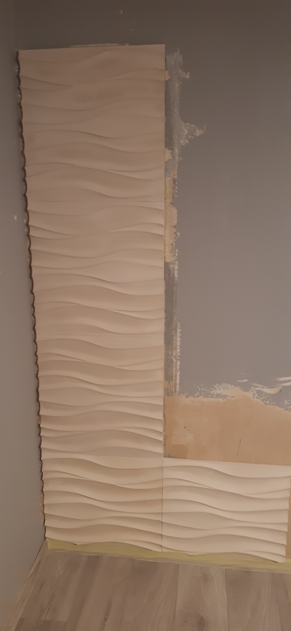 Montaż dekoracyjnych paneli ściennych 3D w narożniku pokoju, widoczne niedoskonałości podłoża przed pełnym wykończeniem.