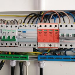 Leszek Lendzion elektryk - Rozdzielnica elektryczna z zamontowanymi zabezpieczeniami przepięciowymi VCX, wyłącznikami nadprądowymi Hager i Gacia, widoczne przewody w kolorach: brązowym, niebieskim, czarnym, żółto-zielonym...