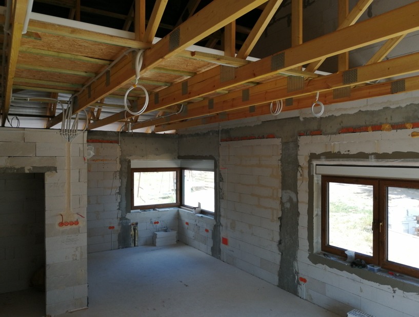 Wnętrze w stanie surowym z widoczną instalacją elektryczną: kable poprowadzone pod drewnianą konstrukcją dachu, puszki elektryczne w ścianach z betonu komórkowego.