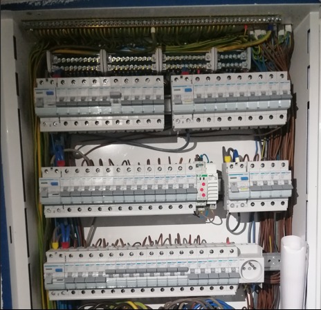 Otwarta szafa elektryczna z licznymi bezpiecznikami, przewodami i listwami zaciskowymi, widok z bliska na instalację elektryczną.