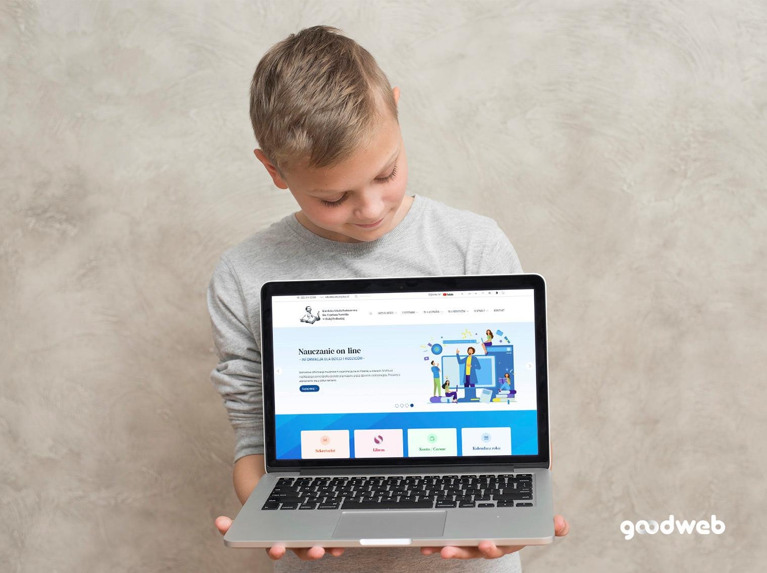 Chłopiec trzyma laptopa prezentującego stronę internetową z niebieską grafiką i napisem 'Nauczanie on line', logo 'goodweb' w prawym dolnym rogu.