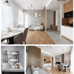 Jasne wnętrze mieszkania z drewnianą podłogą, szarą sofą, białym okrągłym stołem z szarymi krzesłami i aneksem kuchennym z drewnianymi akcentami, oświetlone nowoczesnymi lampami.