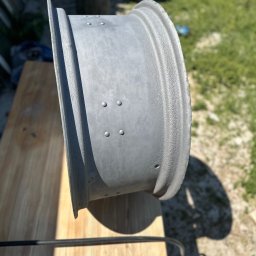 Blp - Szara felga samochodowa po obróbce, leżąca na drewnianym stole w plenerze, widoczne ślady po procesie czyszczenia i przygotowania do malowania.