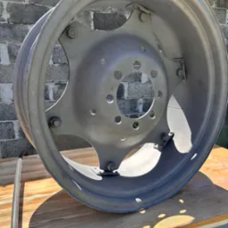 Szara felga samochodowa po piaskowaniu i malowaniu proszkowym, leżąca na drewnianym blacie, z widoczną fakturą betonu w tle.