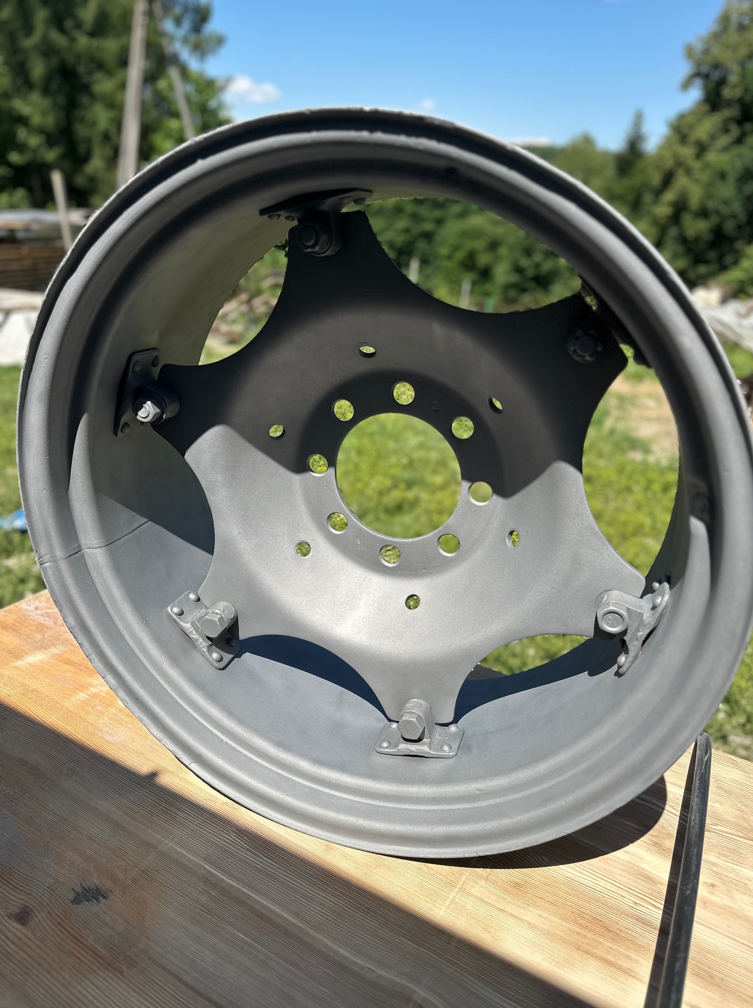 Szara felga koła ciągnika rolniczego po renowacji, leżąca na drewnianym stole w plenerze, widoczne ślady po spawaniu.