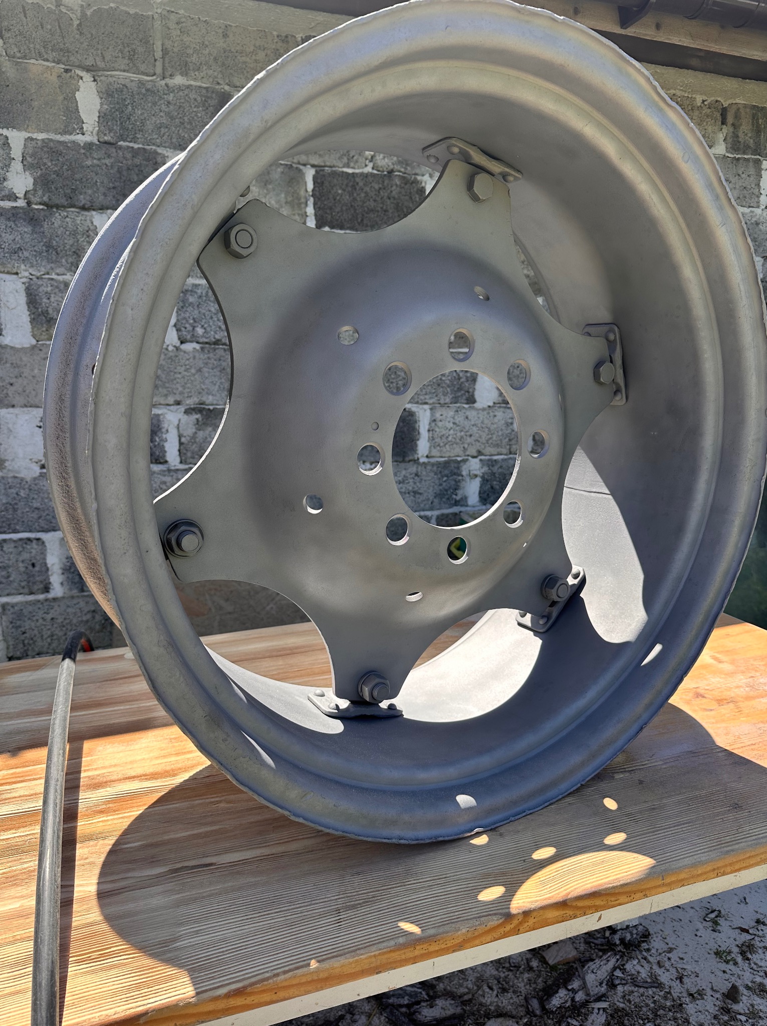 Szara felga samochodowa po piaskowaniu i malowaniu proszkowym, leżąca na drewnianym blacie, z widoczną fakturą betonu w tle.