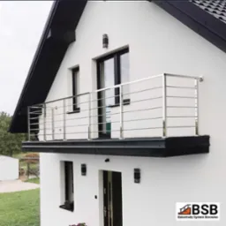 Nowoczesna, pozioma balustrada ze stali nierdzewnej na balkonie domu o białej elewacji i czarnym dachu, widok z dołu.