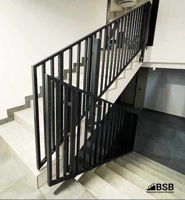 Klatka schodowa z nowoczesną, czarną balustradą o pionowych szczeblach, z widocznym logo firmy w prawym dolnym rogu zdjęcia.