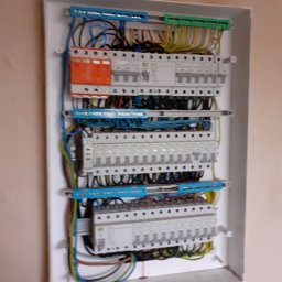 K&A INSTAL BUD - Rozdzielnica elektryczna w białej obudowie, widoczne zabezpieczenia różnicowoprądowe i nadprądowe, przewody ułożone wewnątrz skrzynki, zamontowana na ścianie w trakcie prac wykończeniowych.