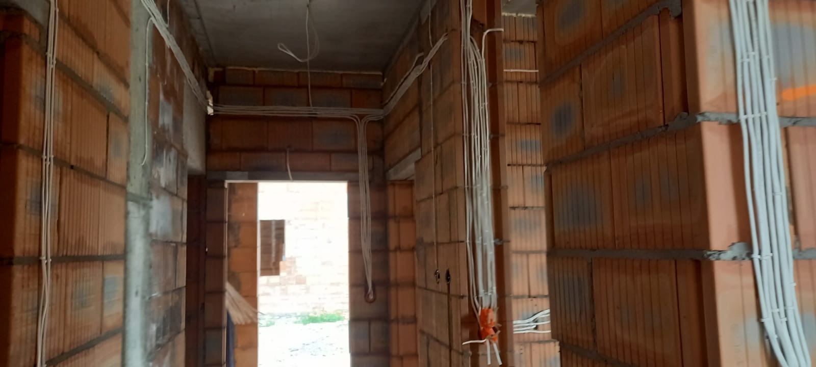 Wnętrze w trakcie budowy z widocznymi przewodami elektrycznymi prowadzonymi w peszlach po ścianach z czerwonej cegły.