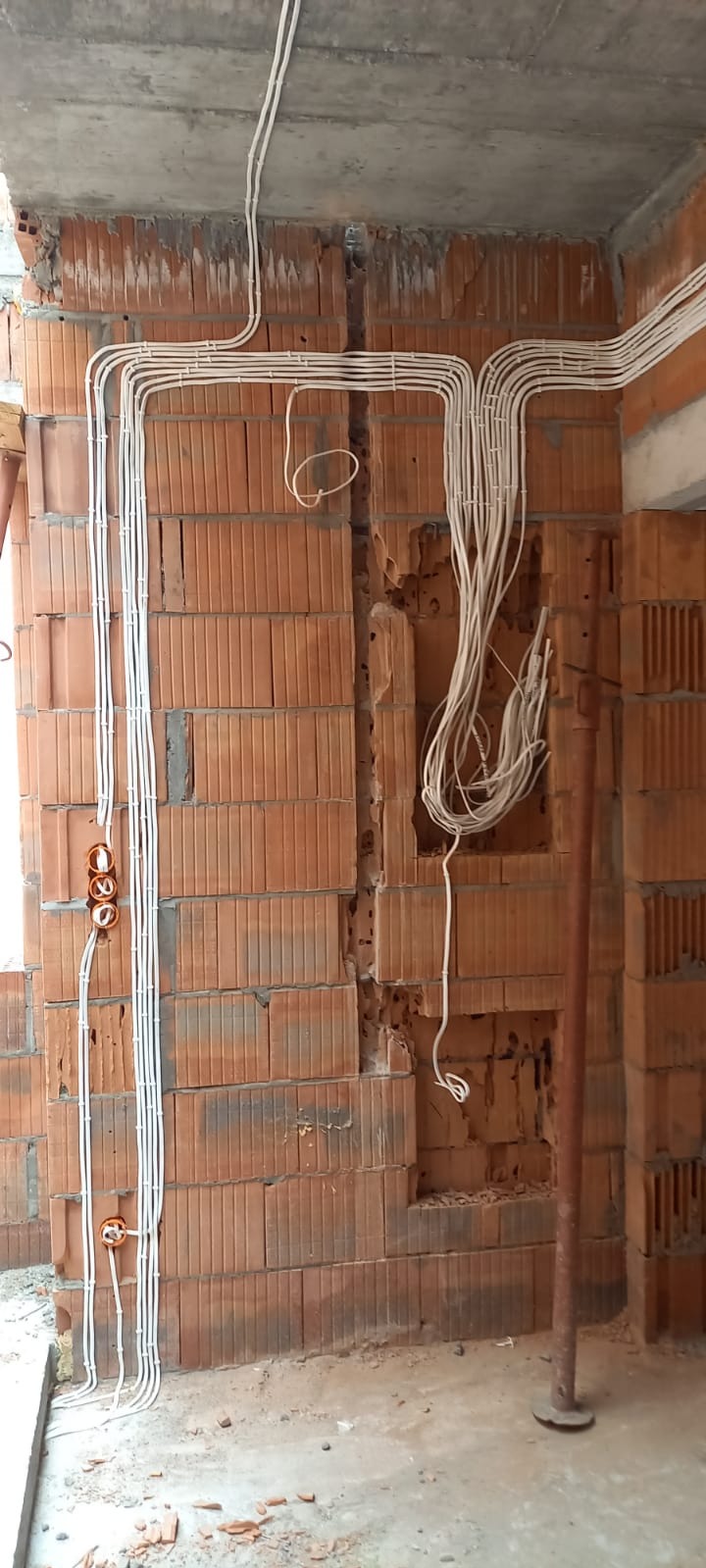 Instalacja elektryczna w trakcie montażu w nowym budynku w Otwocku, widoczne kable prowadzone po ścianie z cegły, puszki instalacyjne zamontowane w ścianie, surowy stan.