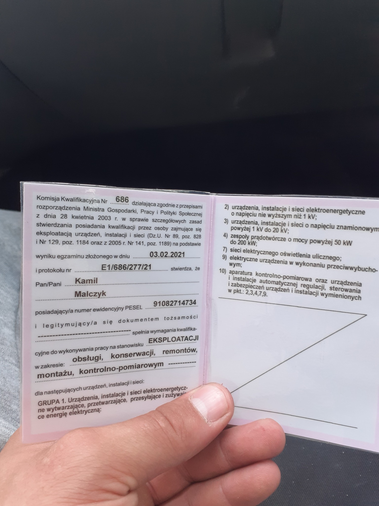 Świadectwo kwalifikacyjne elektryka, uprawniające do eksploatacji urządzeń, instalacji i sieci elektroenergetycznych, trzymane w dłoni.