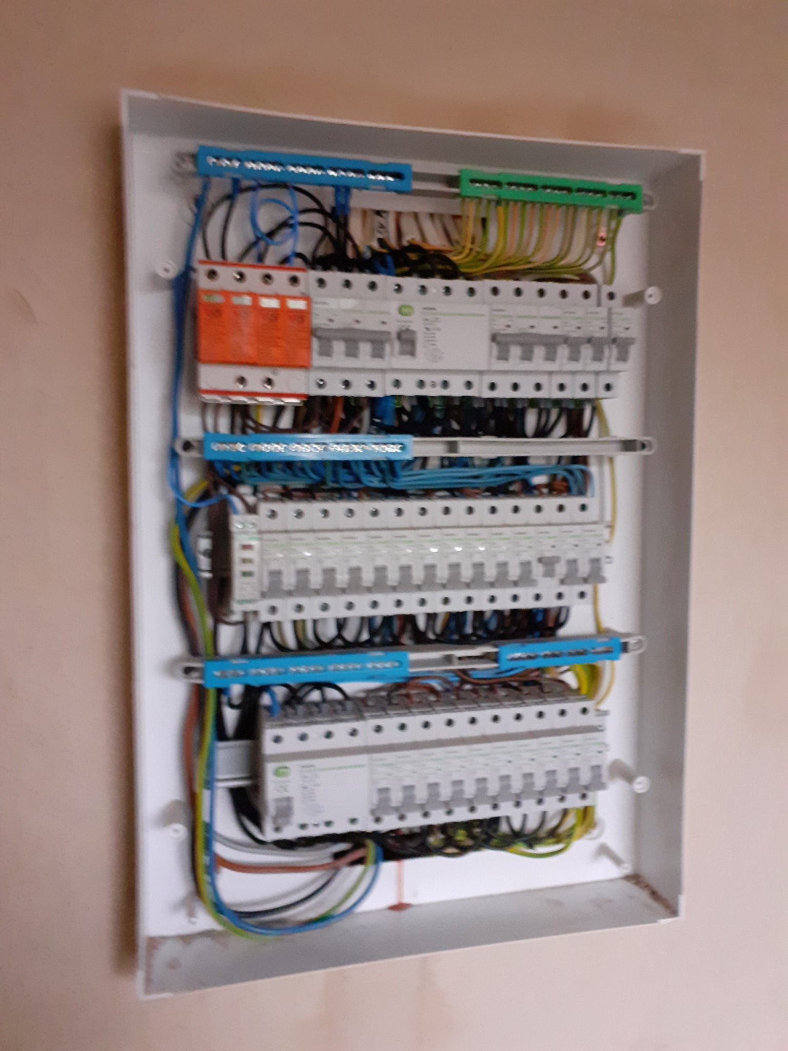 Rozdzielnica elektryczna w białej obudowie, widoczne zabezpieczenia różnicowoprądowe i nadprądowe, przewody ułożone wewnątrz skrzynki, zamontowana na ścianie w trakcie prac wykończeniowych.