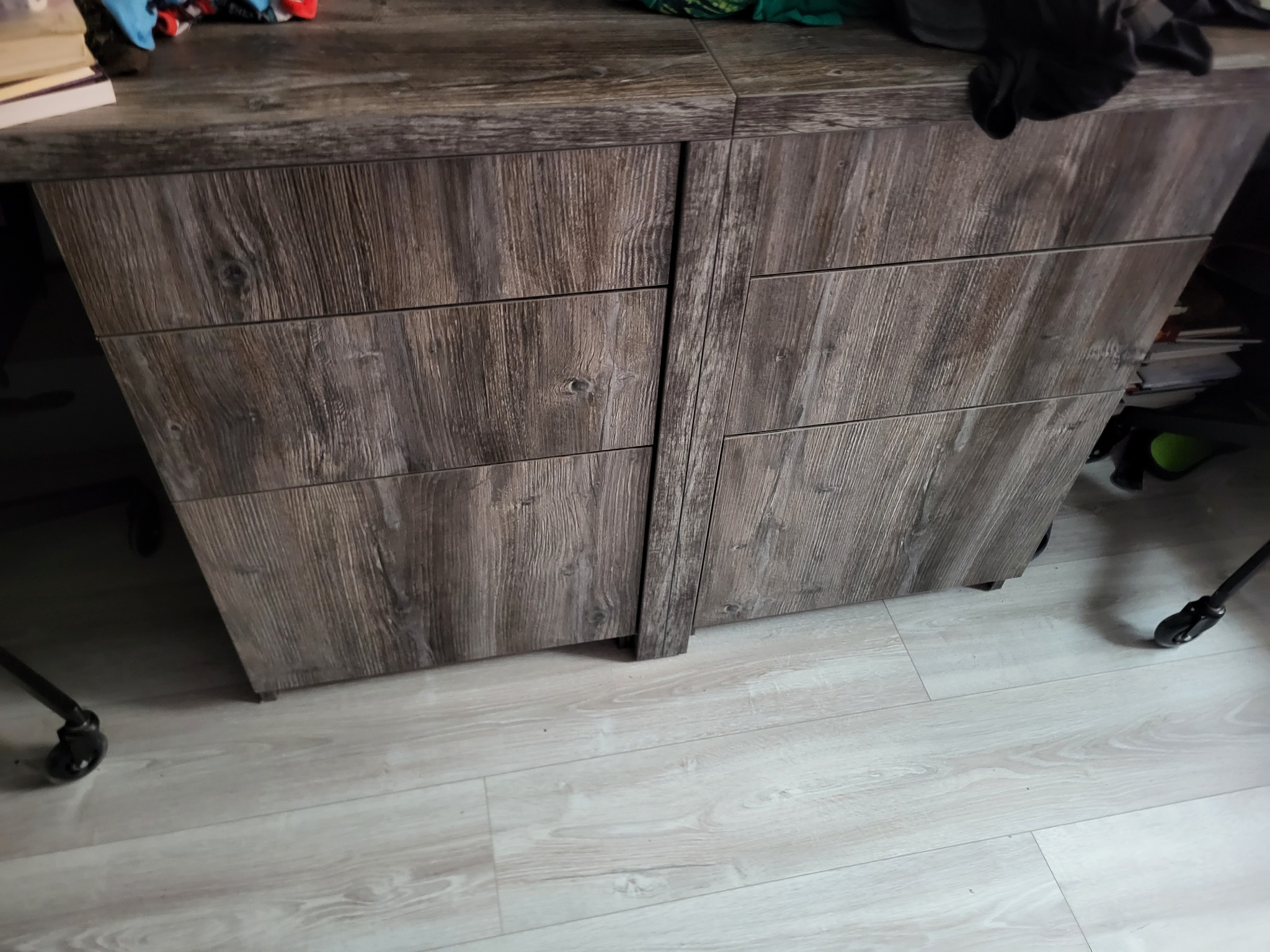 Komoda z szufladami w odcieniach szarości z wyraźną strukturą drewna, widoczne niedoskonałości, ujęcie z niskiego kąta, na blacie widoczne przedmioty.