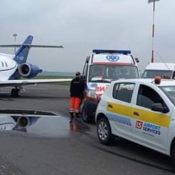 BENE- MED transport medyczny - Obsługa pasażerów na lotnisku: biały prywatny odrzutowiec z otwartymi drzwiami i wysuniętymi schodami, obok ambulans i samochód lotniskowy z logo LS Airport Services na płycie lotniska.