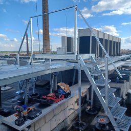 F.H.U. Tomspark - Metalowa konstrukcja schodów i platformy z poręczami na dachu budynku, widoczne narzędzia pracy i urządzenia klimatyzacyjne w tle.