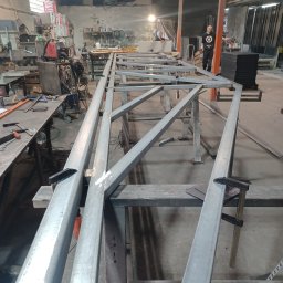 F.H.U. Tomspark - Konstrukcja metalowa z profili zamkniętych w trakcie spawania, widoczne ślady po spawaniu, zaciski stolarskie i narzędzia w tle, warsztat ślusarski.