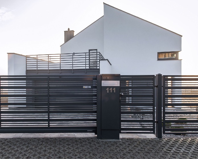 Nowoczesna, pozioma, metalowa brama przesuwna w kolorze antracytowym z numerem domu '111', na tle minimalistycznego, białego domu z płaskim dachem i balustradą na tarasie.