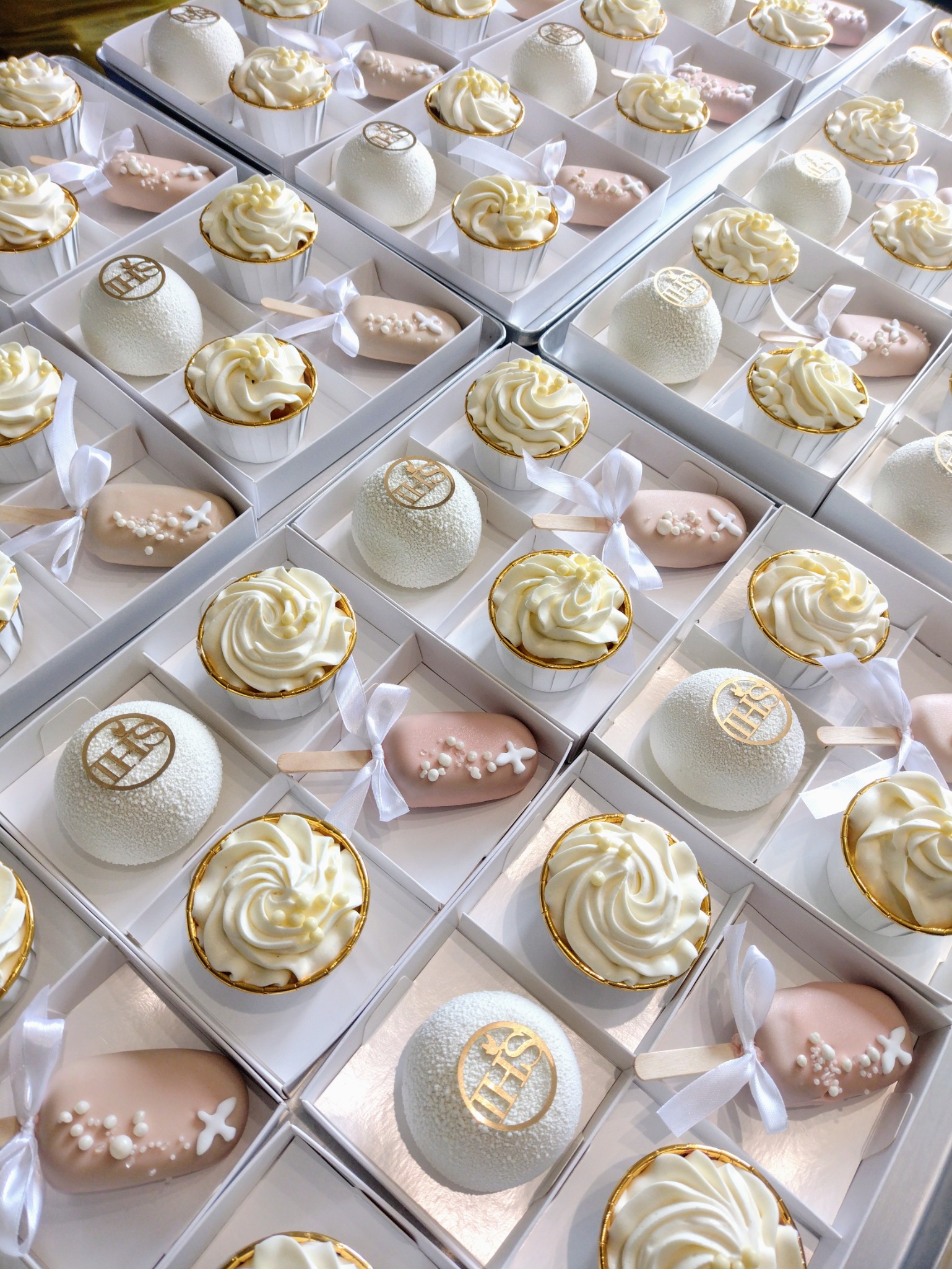 Eleganckie, białe babeczki z kremem, cake pops i desery w pudełkach, idealne na uroczystości. Złote akcenty dodają szyku.