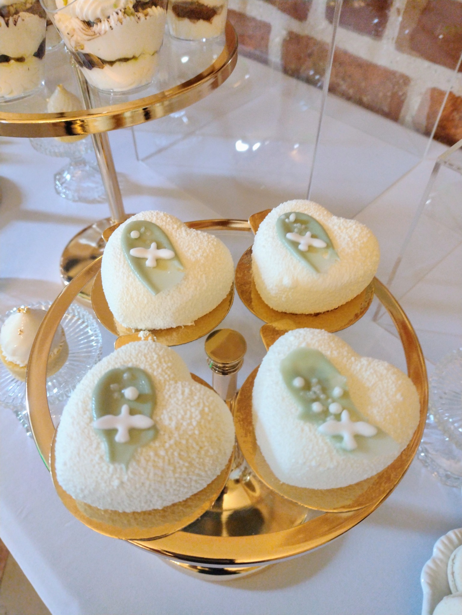 Cztery białe torty w kształcie serca z zielonymi dekoracjami na złotym stojaku, prezentowane na przyjęciu. Eleganckie słodkości na uroczystość.