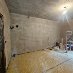 Dominik Róg - Pokój w trakcie prac wykończeniowych: surowe ściany po szpachlowaniu, zabezpieczona folią podłoga, drabina i narzędzia malarskie. Widoczne otwory w ścianie.