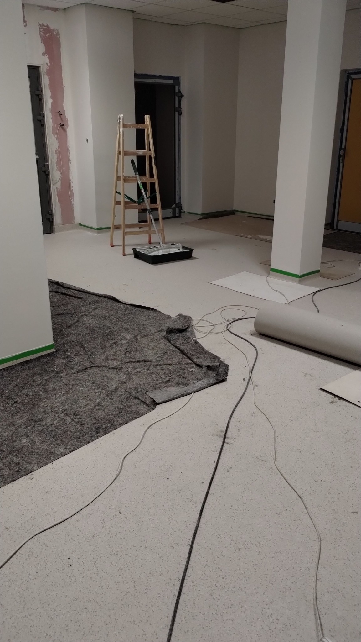 Przygotowania do malowania: drabina, kuweta z farbą, zabezpieczona podłoga i ściany taśmą malarską w jasnym, przestronnym wnętrzu przed dalszymi pracami.