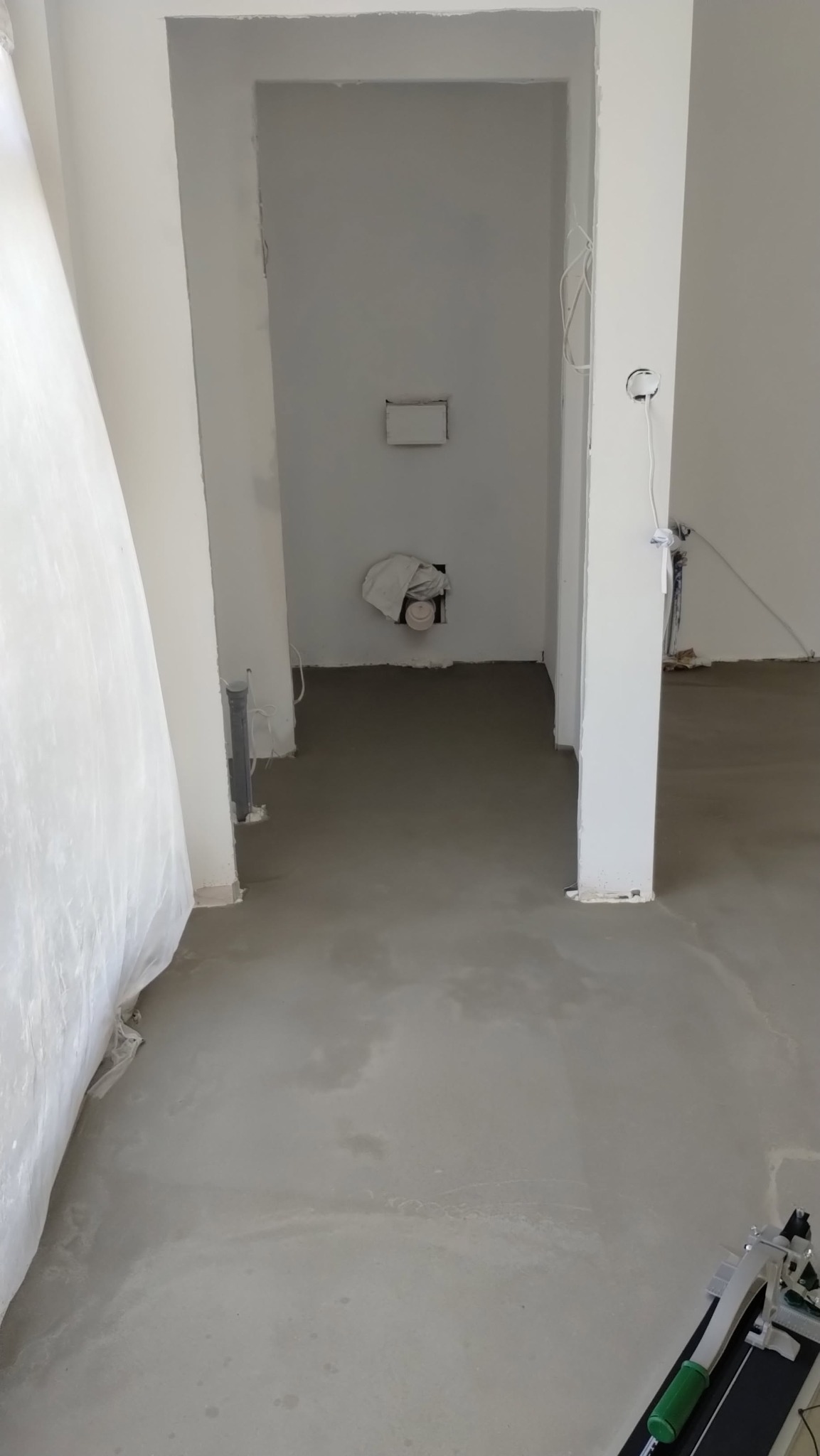 Wnętrze w trakcie remontu: wylana posadzka, przygotowane ściany pod malowanie, widoczne instalacje. Na podłodze narzędzie do cięcia płytek.