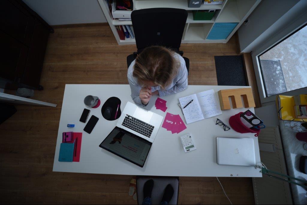 Kobieta siedzi przy biurku z laptopem, notatnikiem i kalkulatorem, analizując dane w biurze z widokiem z góry.